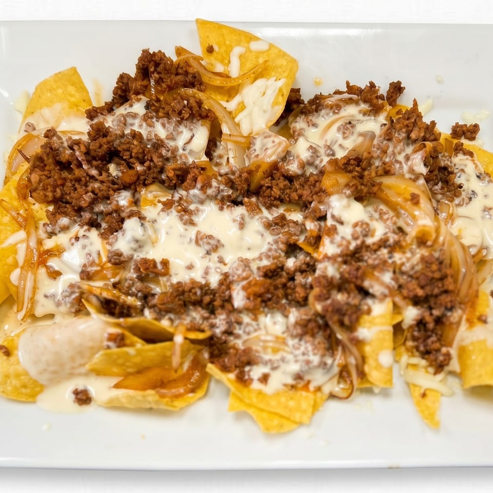 A plate of nachos with ground beef, caramelized onions, and creamy white cheese sauce.